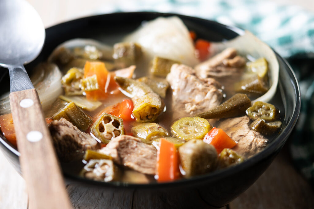 A variety of raw soup bones, including beef and pork, on a wooden cutting board with fresh herbs