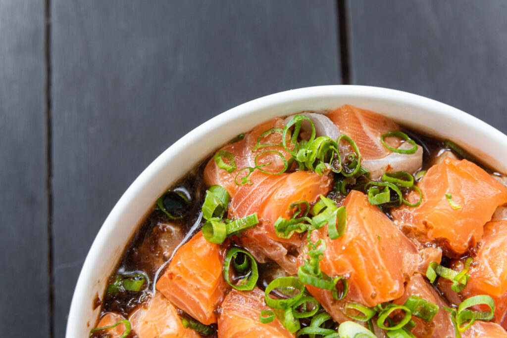 Creamy salmon soup with chunks of salmon, diced carrots, celery, and onions in a creamy broth, garnished with parsley and a drizzle of olive oil.