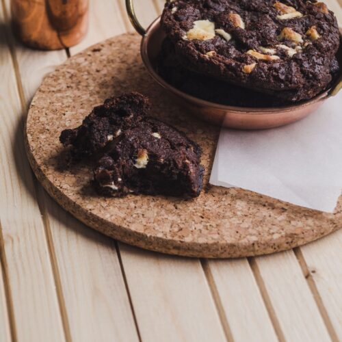 Close-up of a Brownie-Cookie showing a gooey chocolate center and crisp cookie edges, topped with chocolate chips, served on a wooden plate.