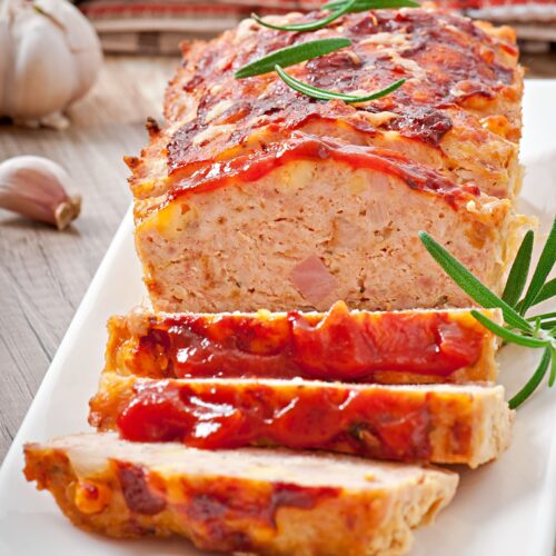 A perfectly smoked meatloaf glazed with BBQ sauce, served on a wooden board with a side of fresh herbs