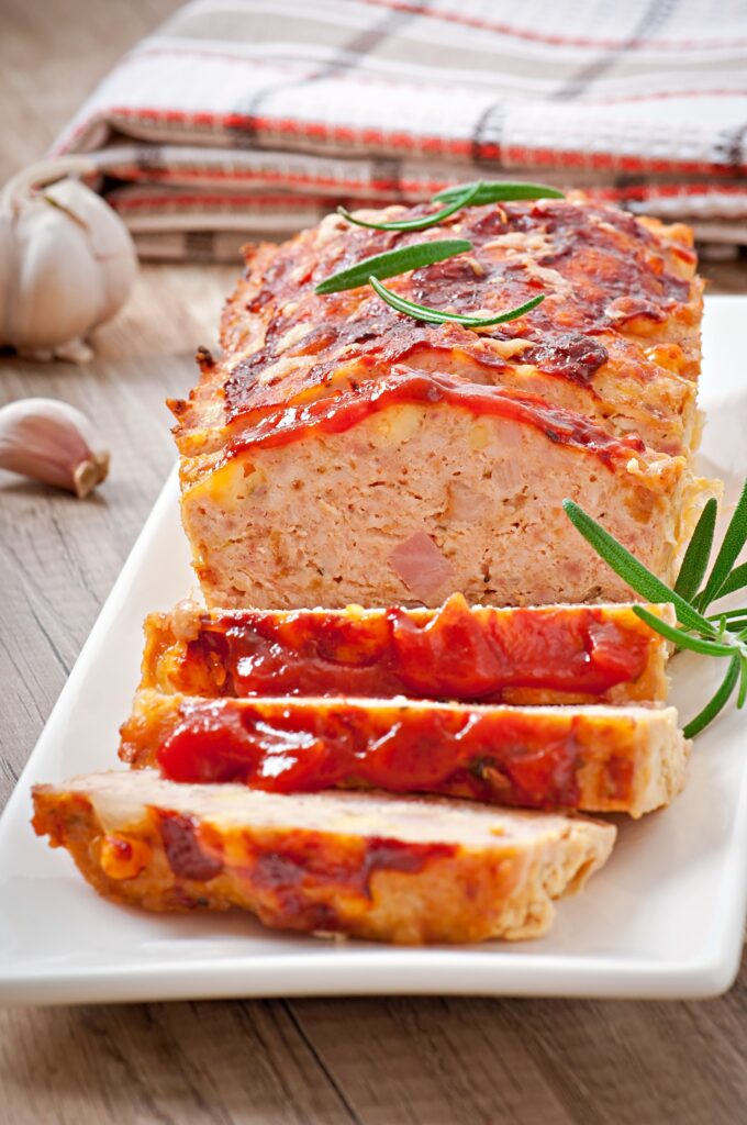 A perfectly smoked meatloaf glazed with BBQ sauce, served on a wooden board with a side of fresh herbs