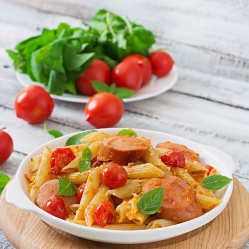 Close-up of tender pasta and sliced smoked sausage coated in a rich, creamy sauce.