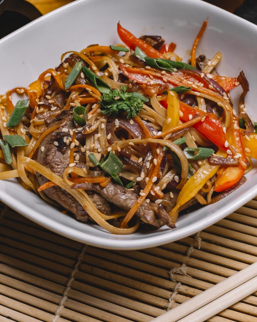 "A beautifully plated Beef Pad Thai served in a shallow bowl, topped with crushed peanuts, lime wedges, and fresh herbs, ready to eat."