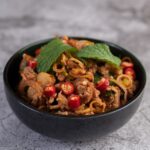 A plate of Beef Pad Thai with tender slices of beef, chewy rice noodles, and garnishes of crushed peanuts, lime wedges, and fresh cilantro.