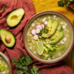 Close-up of traditional Mexican chicken soup with hearty chunks of chicken, diced potatoes, and fresh vegetables, served with a side of warm tortillas and lime wedges.