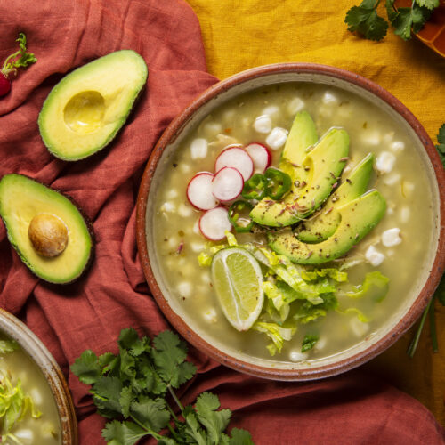 Close-up of traditional Mexican chicken soup with hearty chunks of chicken, diced potatoes, and fresh vegetables, served with a side of warm tortillas and lime wedges.