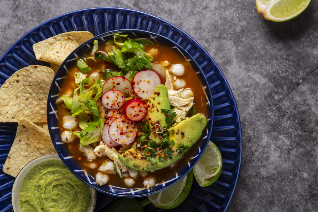 Hearty and healthy Mexican chicken soup in a rustic bowl, filled with shredded chicken, corn, potatoes, and zucchini, topped with fresh avocado and a sprinkle of queso fresco.