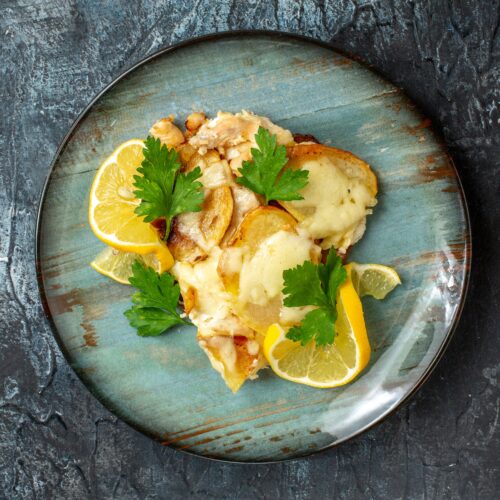 A plate of golden-seared scallops served over creamy lemon butter orzo, garnished with fresh parsley and a lemon wedge.