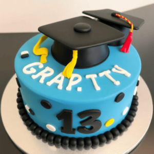 A round cake decorated with a black fondant graduation cap, a yellow tassel, and piped frosting reading 'Congratulations!' in bold letters